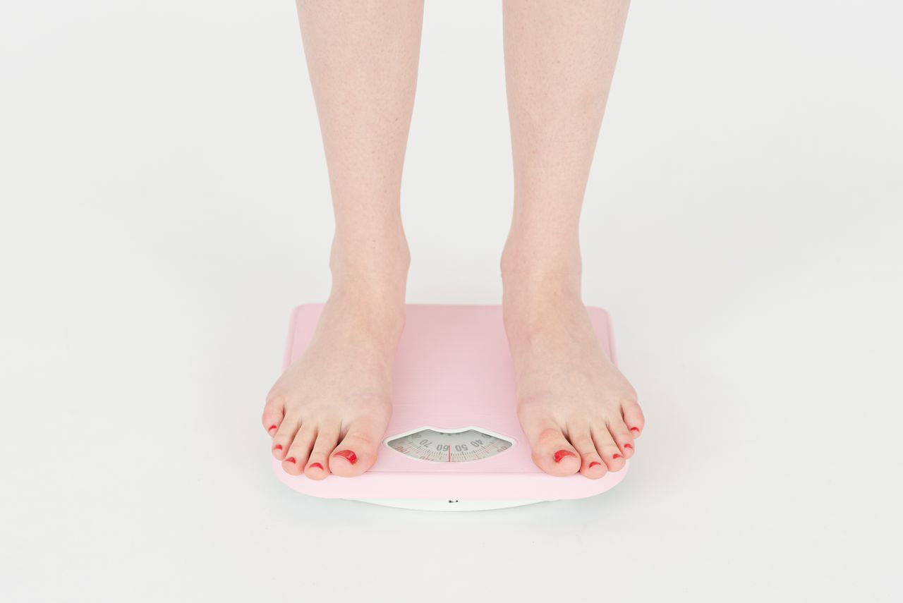 High angle of crop anonymous female measuring weight for control body against white background in studio